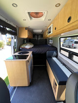 Bright RV rental interior features a kitchen, cozy bed, bench seating, and wood cabinets for comfortable travel.