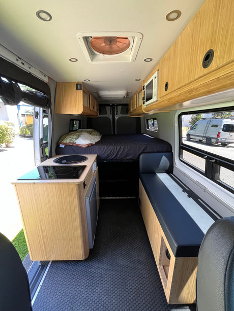 Bright RV rental interior features a kitchen, cozy bed, bench seating, and wood cabinets for comfortable travel.