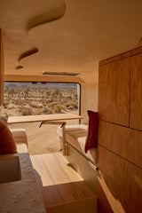 RV rental interior: light wood, pull-out table, sculpted ceiling, and a panoramic desert view with Joshua trees.