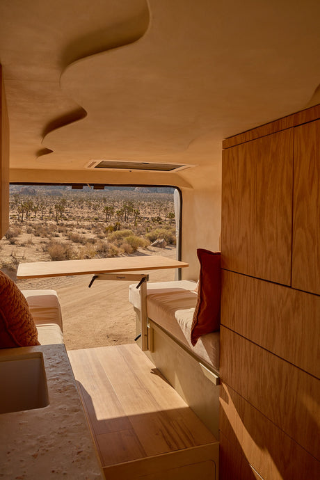 RV rental interior: light wood, pull-out table, sculpted ceiling, and a panoramic desert view with Joshua trees.