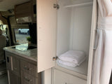 RV rental compact kitchen featuring a stovetop, organized storage cabinet with fresh towels, and a curtain.