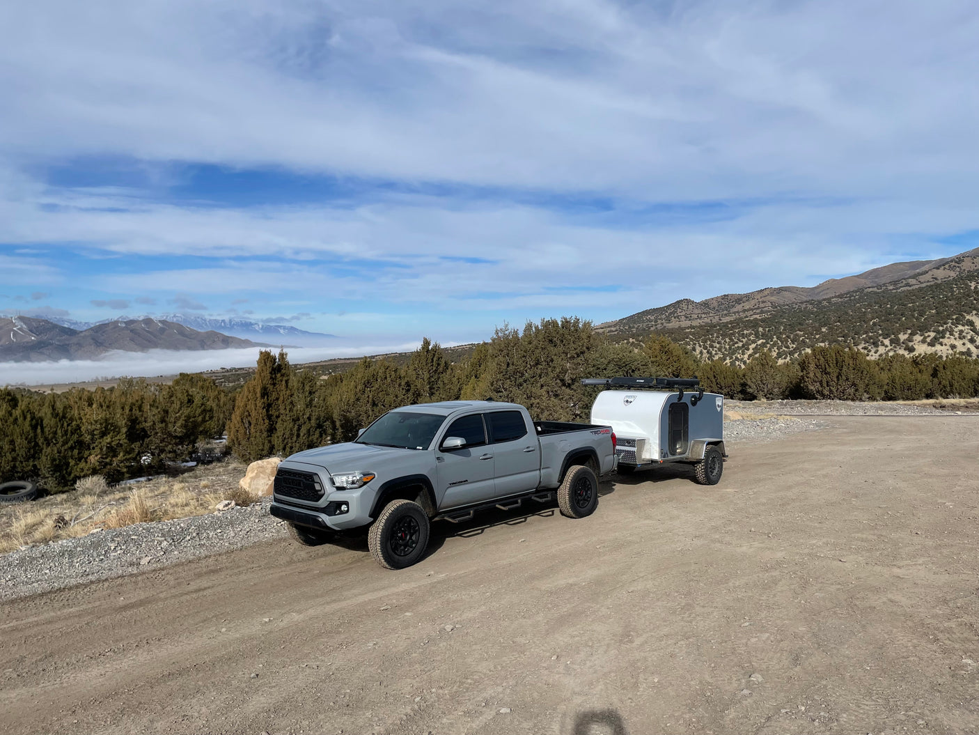 Grey Toyota Tacoma truck towing an overland camper on a dirt road. Mountains & fog in background. Perfect RV rental setup!