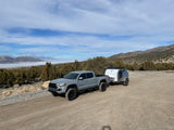 Grey Toyota Tacoma truck towing an overland camper on a dirt road. Mountains & fog in background. Perfect RV rental setup!