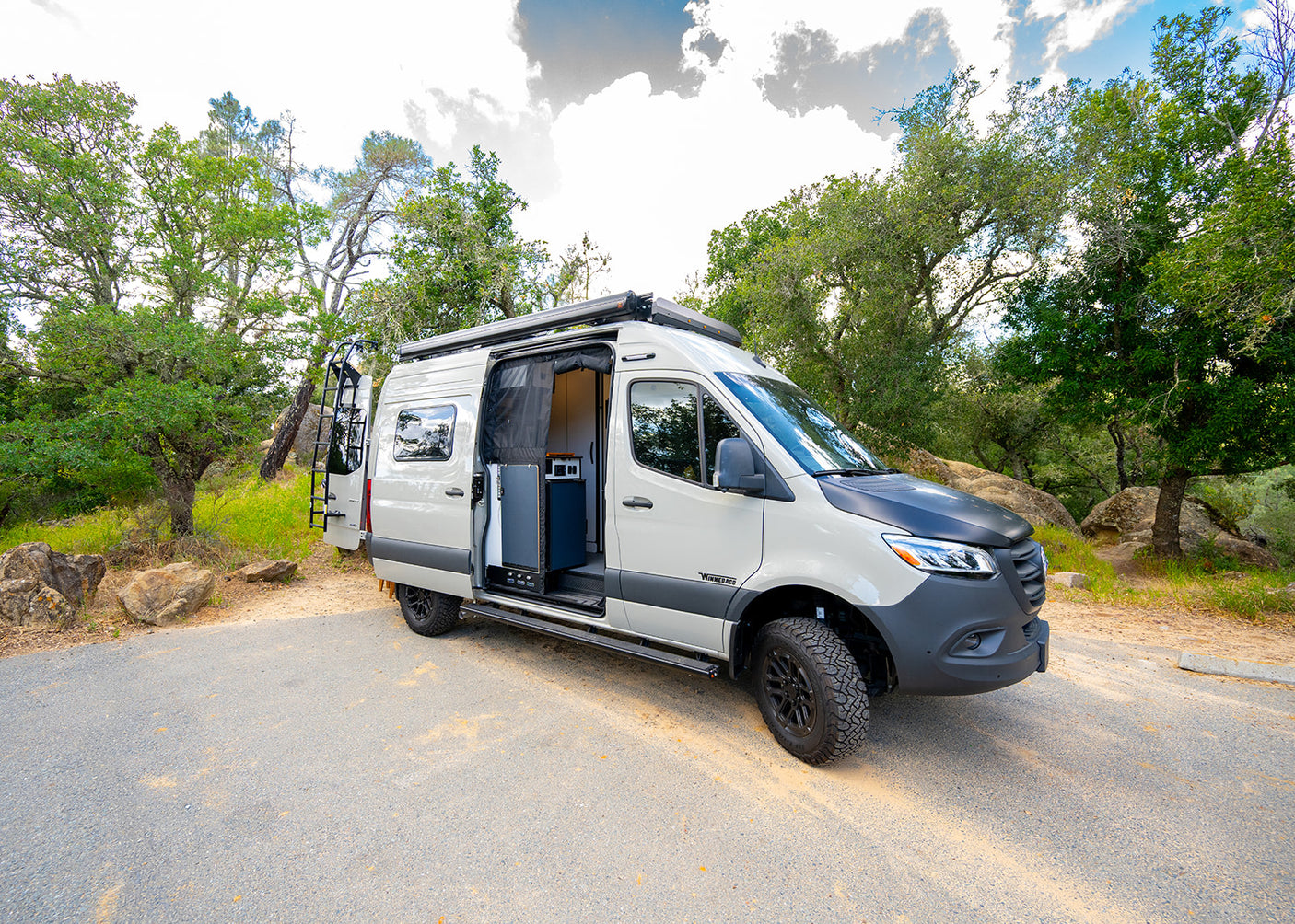 This Winnebago camper van, ideal for rv rental adventures, is parked in a scenic natural setting with its side door open, showing the interior.