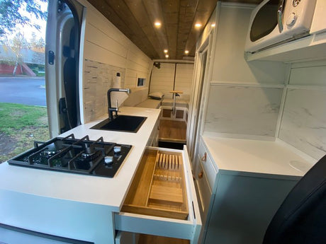 Bright RV rental interior showing a modern kitchen with gas stove, sink, microwave, and utensil drawer. Ideal for road trips.