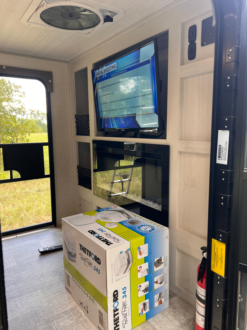 Inside an RV rental, a TV, electric fireplace, and a boxed Thetford Porta Potti 345 sit near the open door. — photo 7