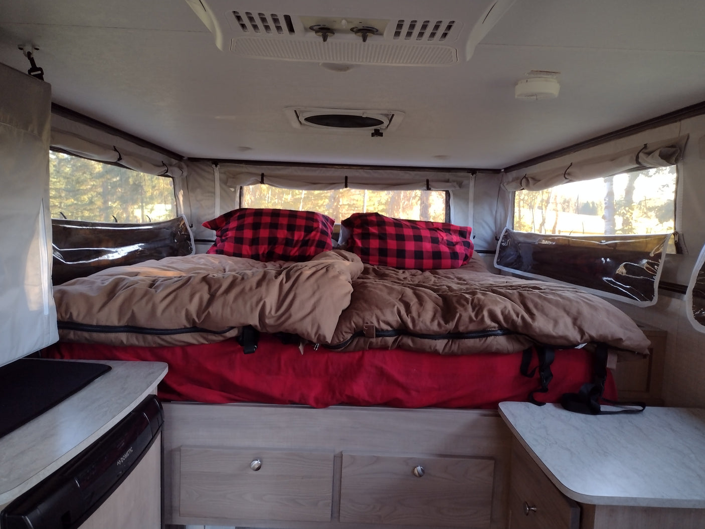 Inside a cozy RV rental: a bed with buffalo check pillows & bright windows. Perfect for camping!