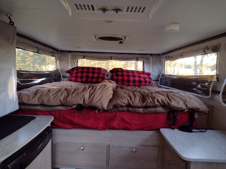 Inside a cozy RV rental: a bed with buffalo check pillows & bright windows. Perfect for camping!