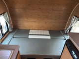 RV rental interior: wood-paneled walls, gray & white convertible bed/seating, striped curtains, sink, & Dometic fridge.