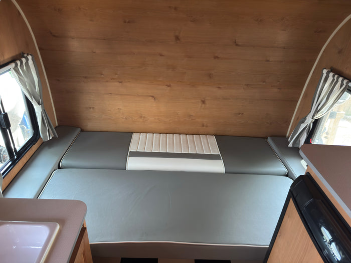 RV rental interior: wood-paneled walls, gray & white convertible bed/seating, striped curtains, sink, & Dometic fridge.