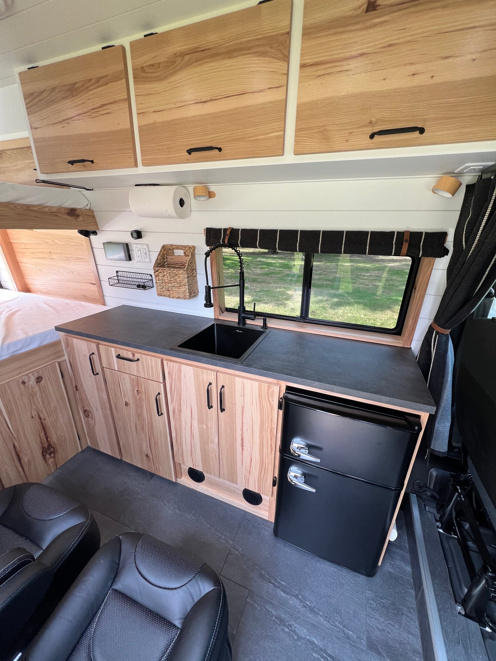 RV rental: Modern camper van interior with kitchenette, black sink, wood cabinets, mini fridge, bed, and seating.