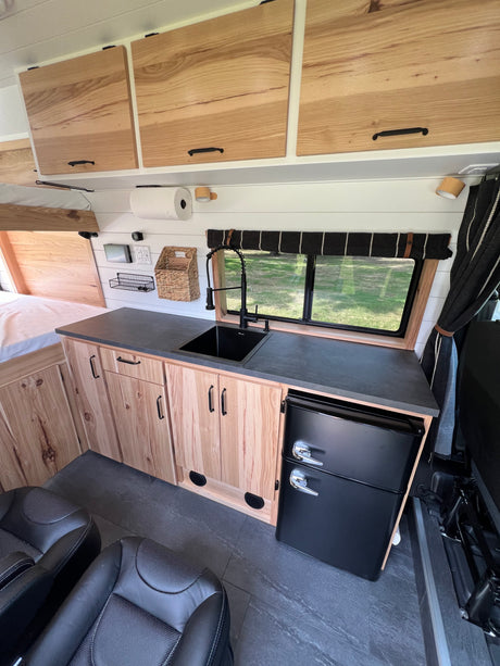 RV rental: Modern camper van interior with kitchenette, black sink, wood cabinets, mini fridge, bed, and seating.