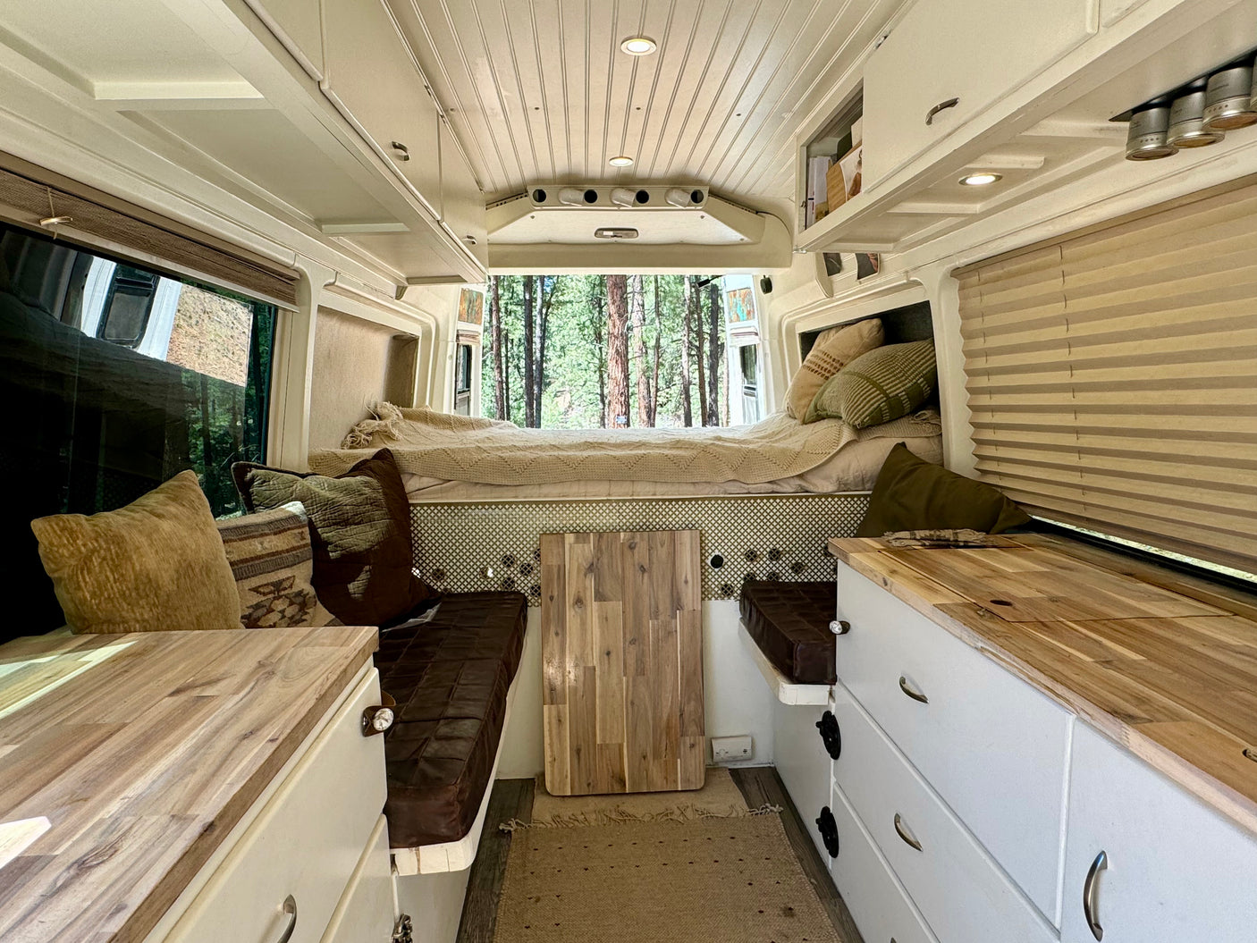 Experience nature from this cozy RV rental's custom interior, featuring a bed, seating, and panoramic forest views.