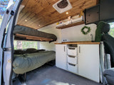 Comfy rv rental van interior: wooden ceiling, upper & lower beds, plus a compact kitchen with wood counters & tiled backsplash.