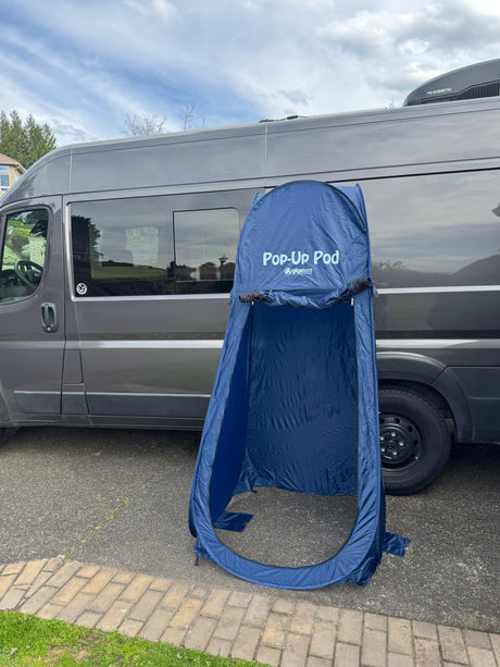 Dark gray camper van with blue 'Pop-Up Pod' tent on driveway. Portable privacy for your RV rental outdoor trip.