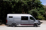 This grey custom Mercedes Sprinter van, an 'Endeavor' rv rental, is parked roadside surrounded by green trees.