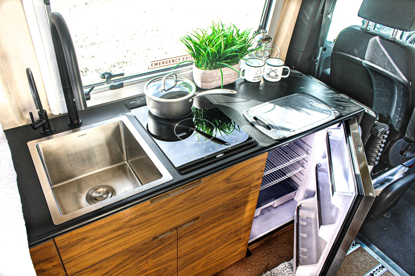 Compact kitchen in an RV rental with stainless steel sink, induction cooktop, and open refrigerator. — photo 9