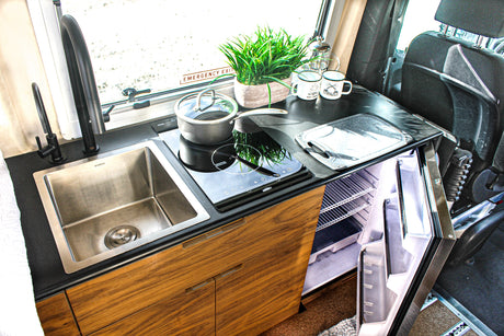 Compact kitchen in an RV rental with stainless steel sink, induction cooktop, and open refrigerator.