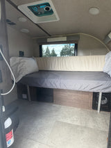 This cozy rv rental interior showcases a bed, window with nature views, ceiling fan, and fire extinguisher. Ready for travel!