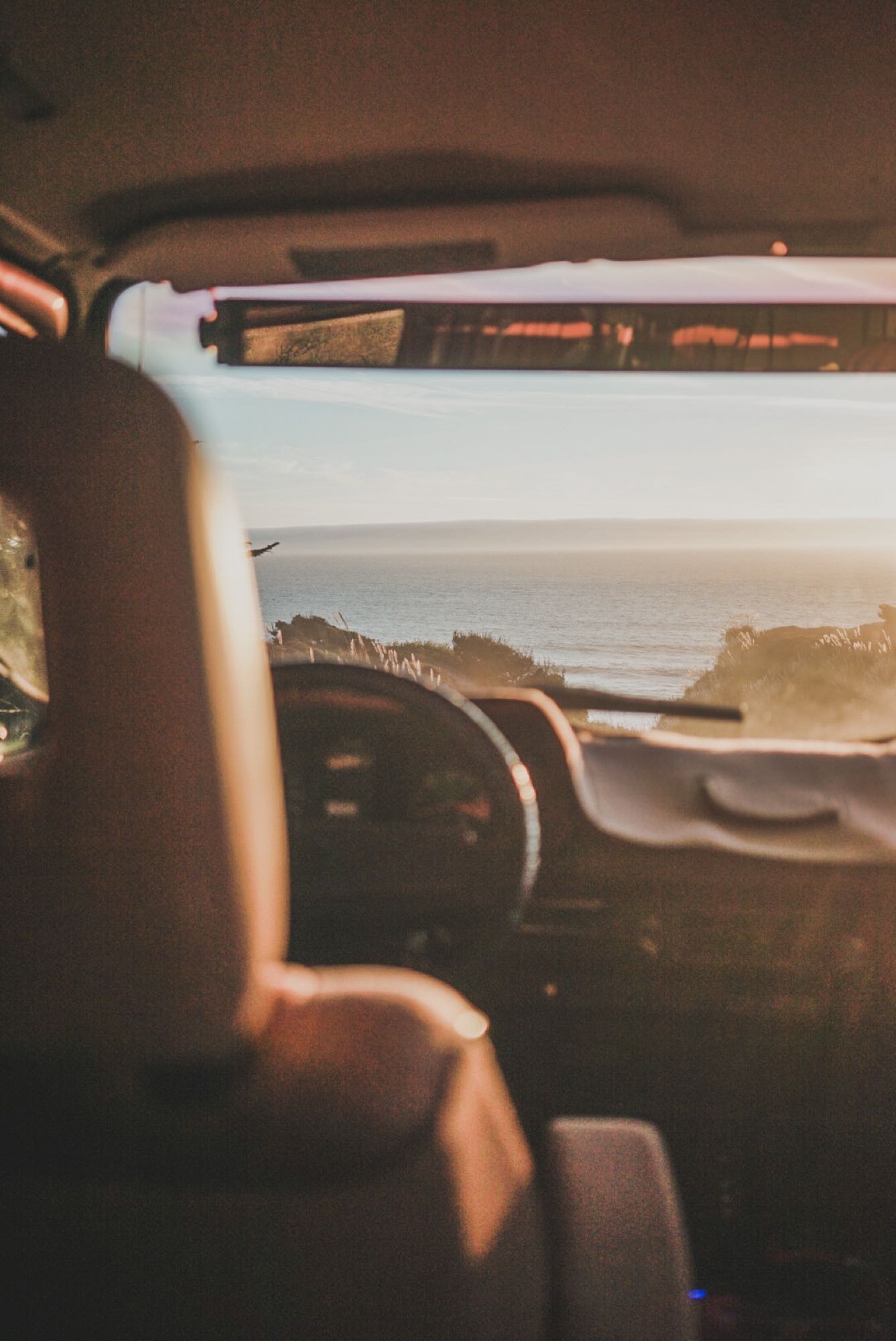  and a bright ocean sunset view from the rear.|View from an RV rental dashboard showing a sunlit ocean and coastline. Interior seat on left — photo 7