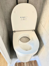 Inside an RV rental: a compact Separett composting toilet with a urine diversion feature, set against gray tiles and wood flooring.