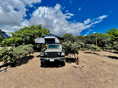 Gray Jeep Wrangler with a Thule rooftop tent, perfect for an RV rental adventure in a lush Hawaii campsite.