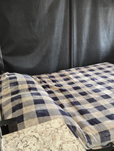 Cozy RV rental interior: A bed with a blue and beige plaid blanket rests against a dark fabric wall, next to a marble-look countertop.