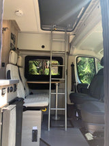 This cozy camper van interior is perfect for your next RV rental adventure, featuring a dining area, bed, and ladder to an upper bunk for mobile living.