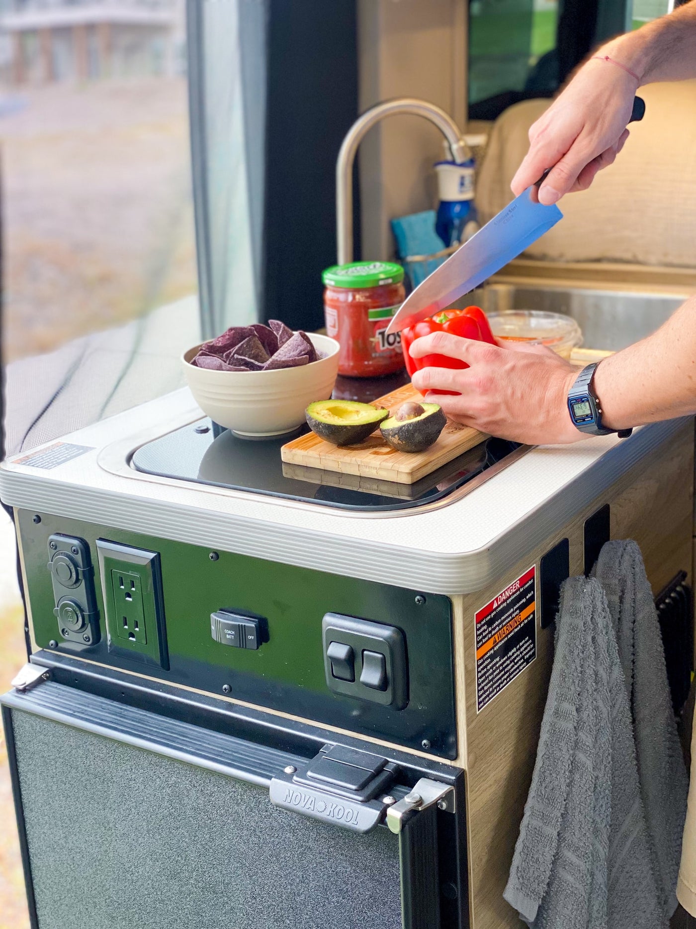 Prepping fresh ingredients in an RV rental kitchen: hands slice bell pepper, avocados, with chips, salsa, sink, and Nova Kool fridge. — photo 16