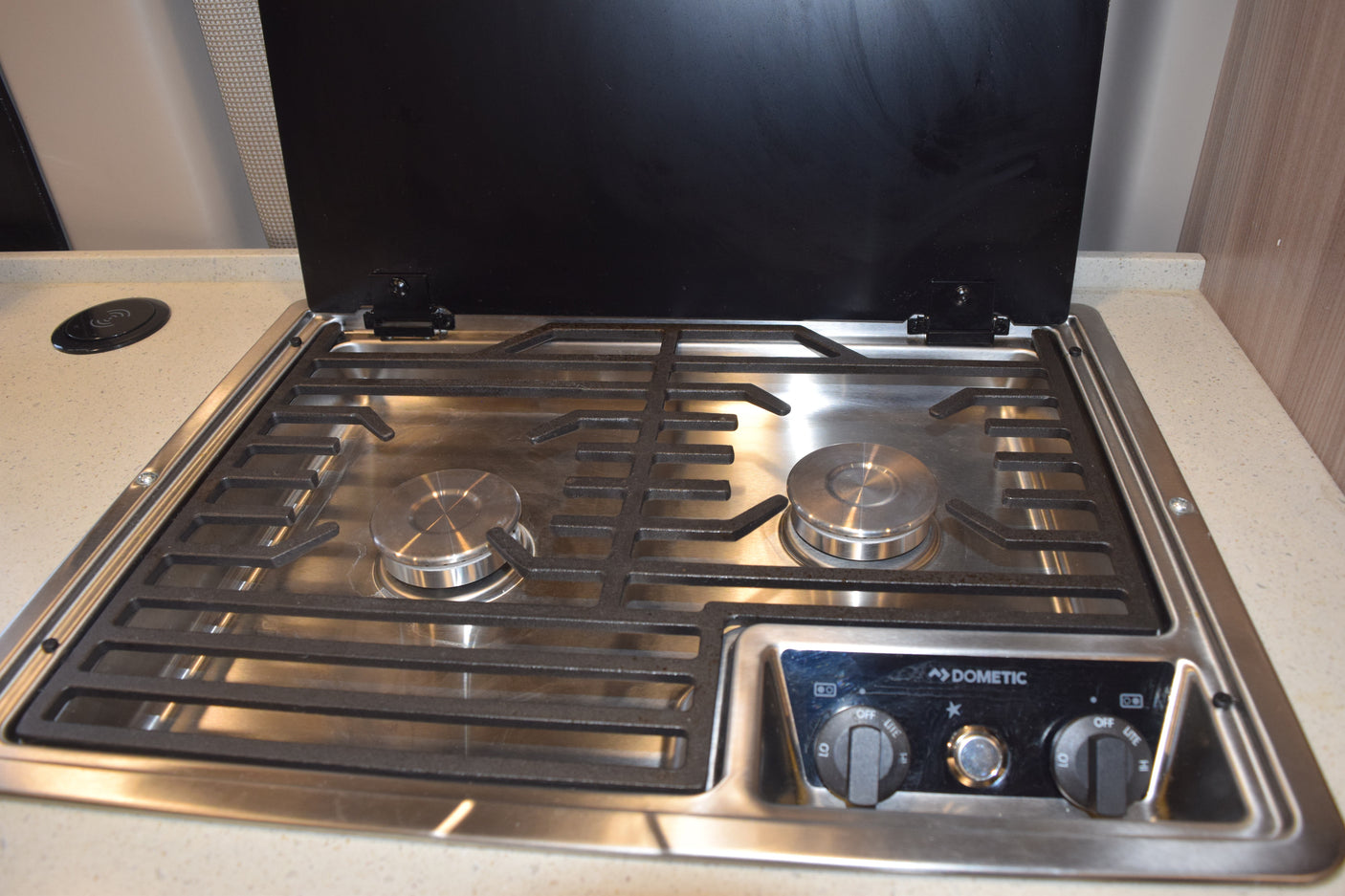 RV rental kitchen: Dometic stainless steel gas stovetop with two burners, controls, and a wireless charger on the counter.