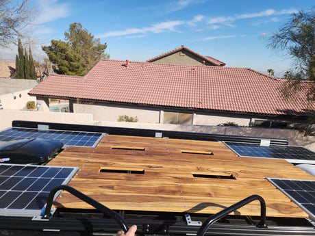 View from an RV rental rooftop, showcasing solar panels, a wooden deck, and residential homes under a clear sky.
