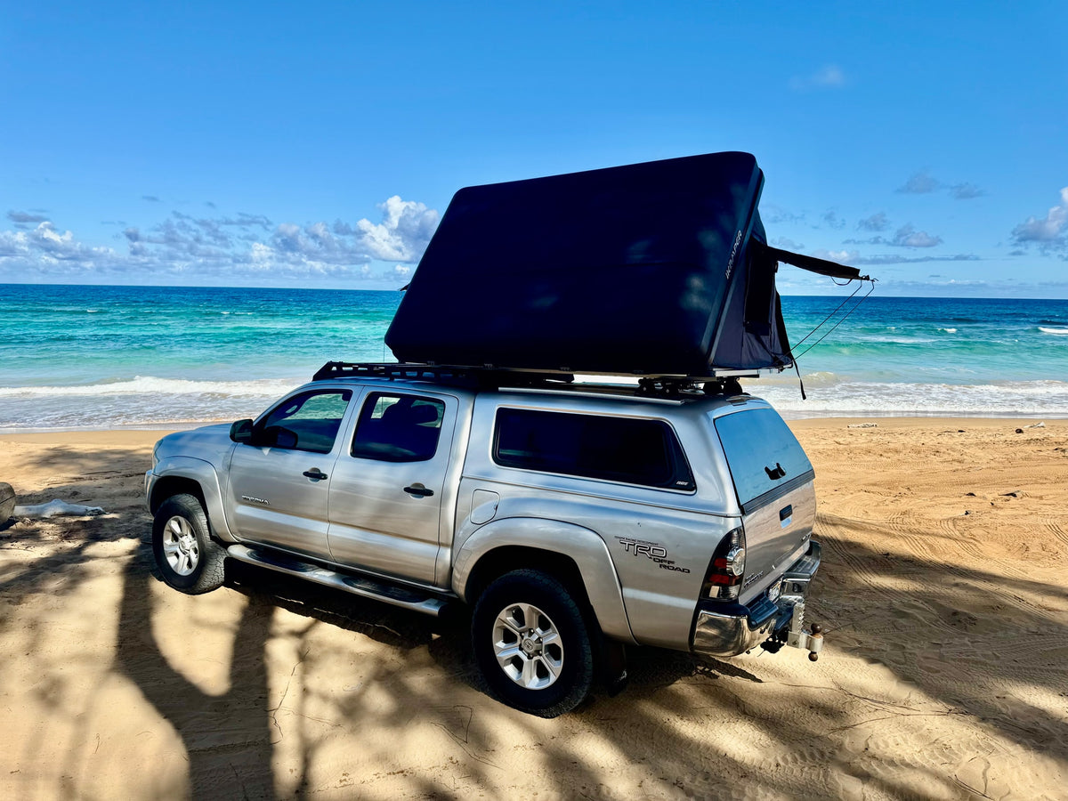 Silver Tacoma truck with rooftop tent parked on a sunny beach near the blue ocean. A great RV rental alternative for adventures. — photo 2