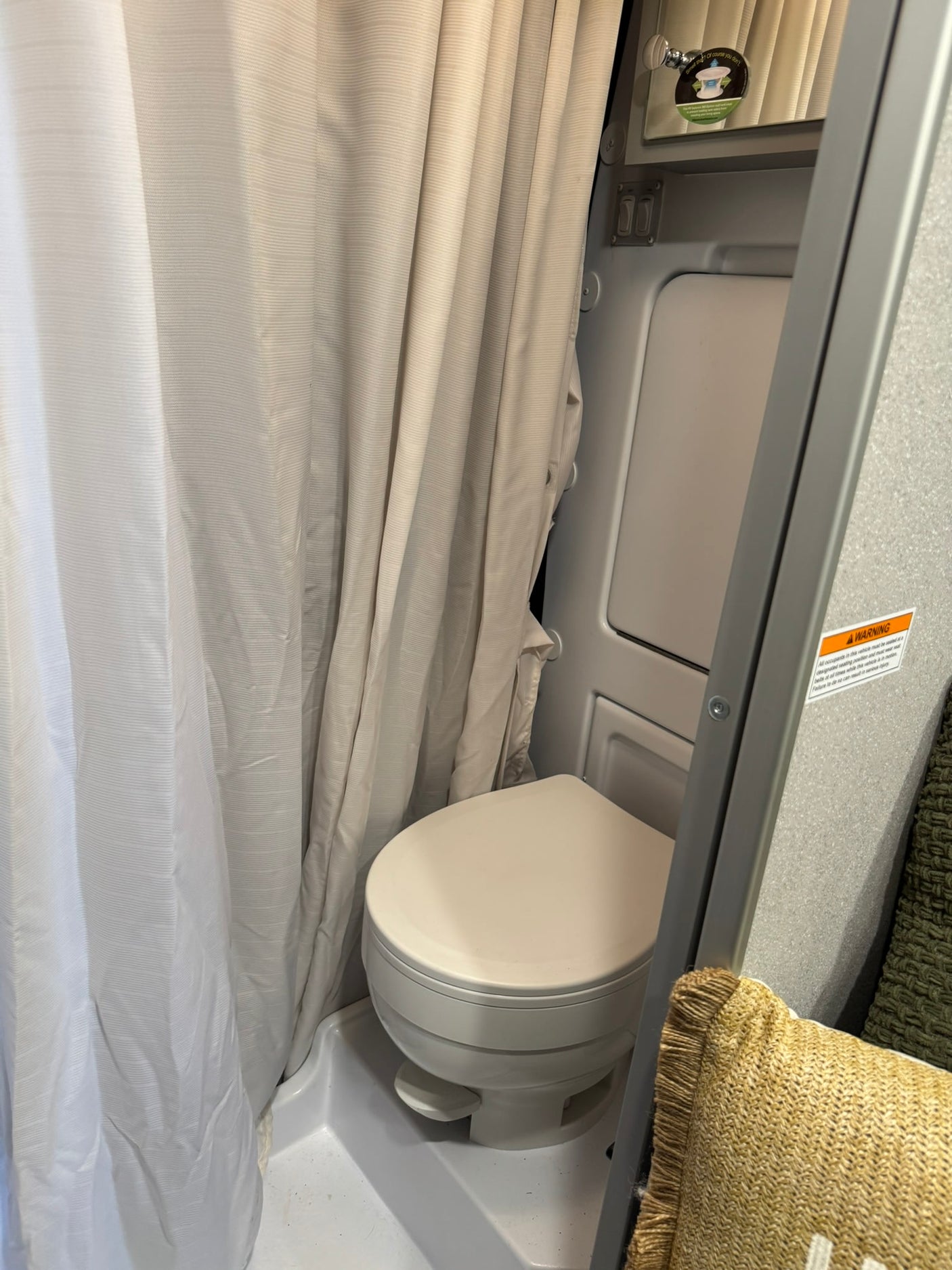 This compact RV rental bathroom includes a toilet, shower curtain, and mirror, designed for efficient use of space.