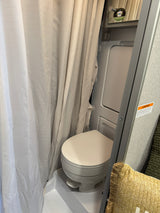 This compact RV rental bathroom includes a toilet, shower curtain, and mirror, designed for efficient use of space.