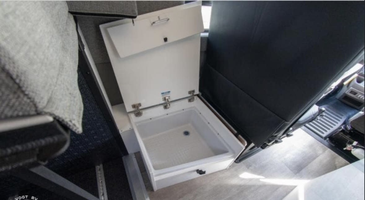 Inside an RV rental, an open white cooler/storage bin with a drain is shown, positioned next to dark seating and light flooring.