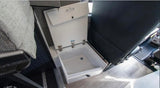 Inside an RV rental, an open white cooler/storage bin with a drain is shown, positioned next to dark seating and light flooring.