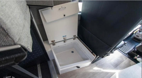 Inside an RV rental, an open white cooler/storage bin with a drain is shown, positioned next to dark seating and light flooring.