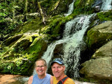 Smiling couple by a beautiful waterfall amidst green rocks. An RV rental trip offers great outdoor adventures!
