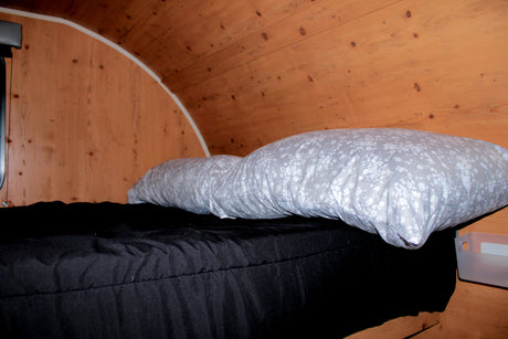 This rv rental features a cozy sleeping area with dark bedding, floral pillows, and a curved wooden ceiling.