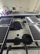 Overhead view of an RV rental van's roof, featuring four solar panels on a robust rack system and a roof vent.