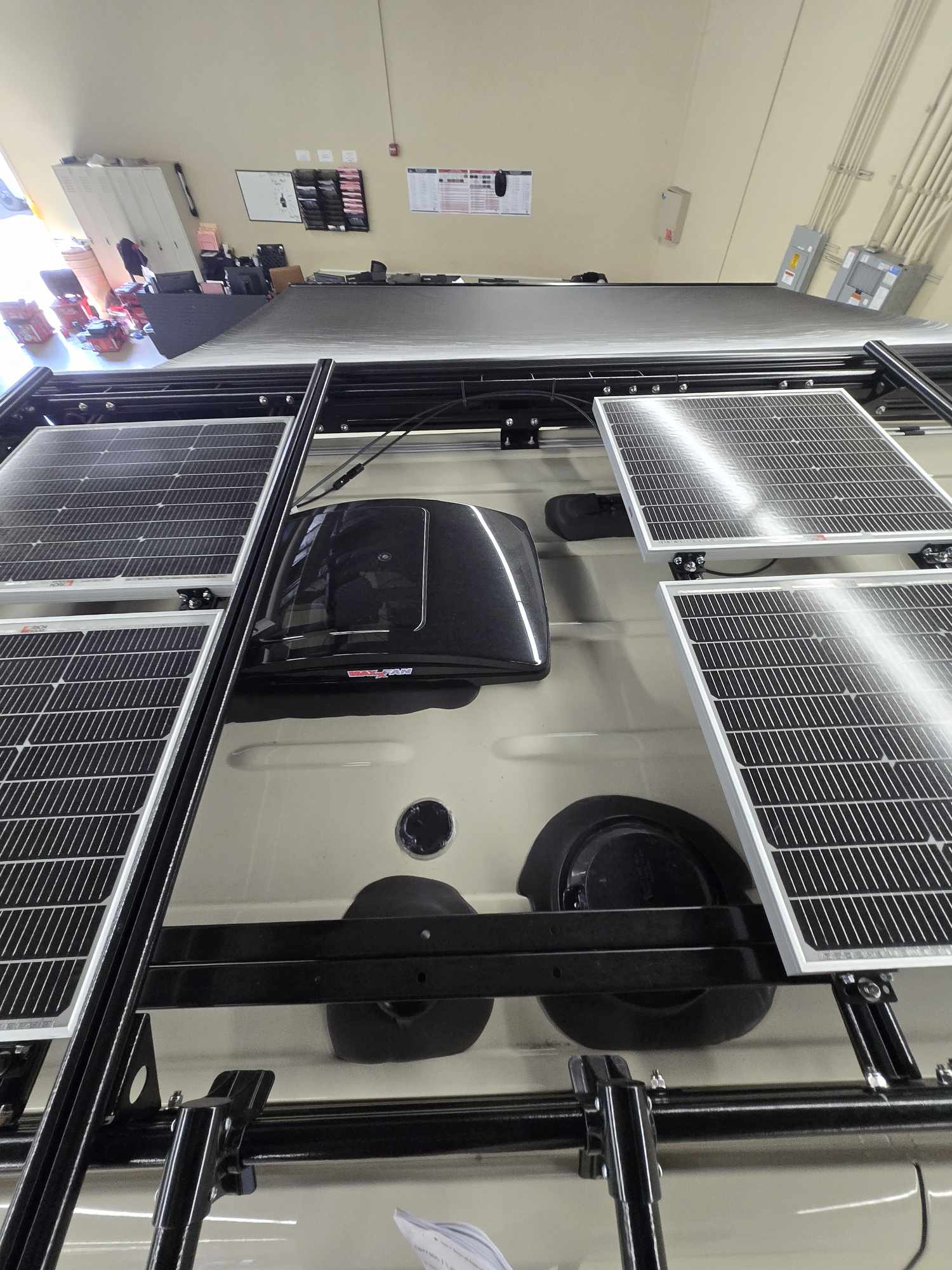 Overhead view of an RV rental van's roof, featuring four solar panels on a robust rack system and a roof vent.