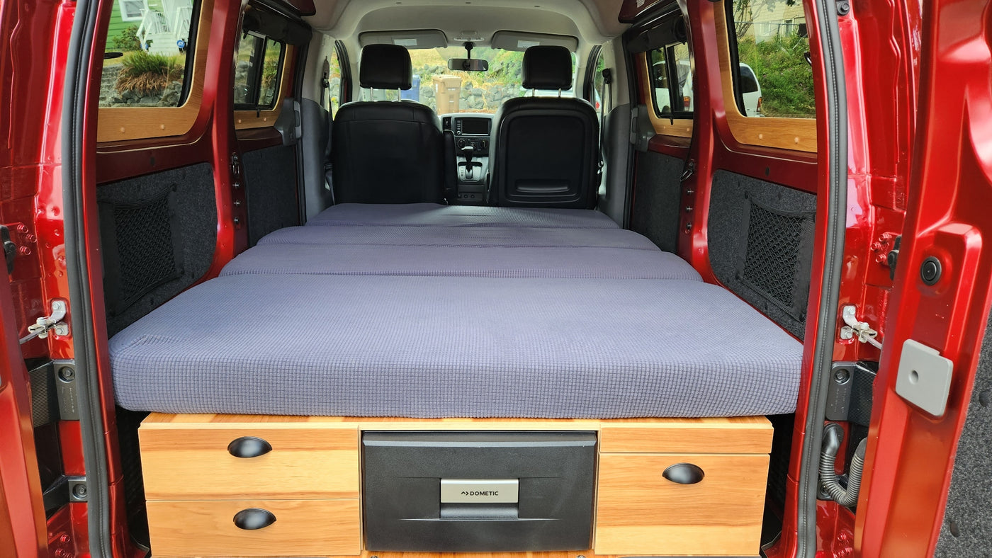 Red camper van's cozy interior, featuring a grey mattress bed, wooden storage, and a Dometic fridge, ideal for rv rental. — photo 13
