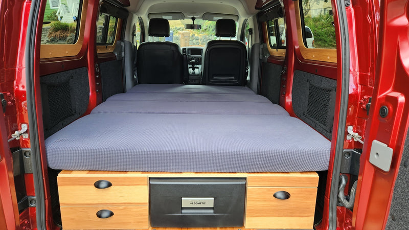 Red camper van's cozy interior, featuring a grey mattress bed, wooden storage, and a Dometic fridge, ideal for rv rental. — photo 13