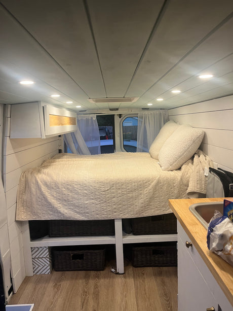 Experience van life in this cozy rv rental! Features a comfortable bed, kitchen area, and organized storage inside.