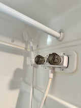 An RV rental's compact shower interior, featuring white walls, a two-handle faucet, and a handheld shower head.