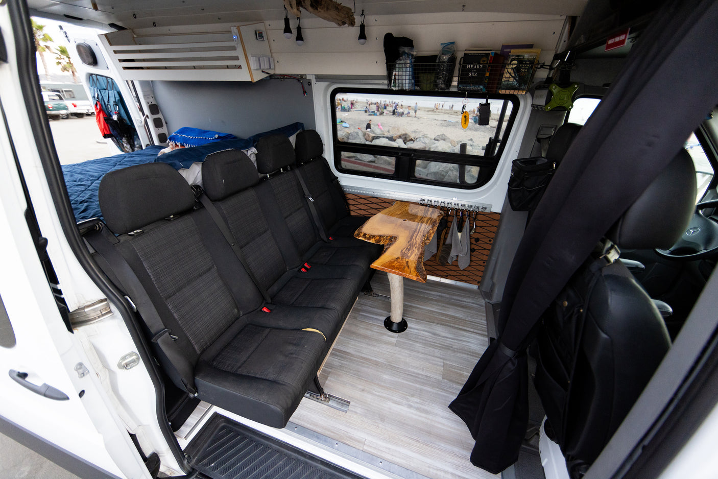 Inside a comfortable RV rental: custom van conversion with bench seats, dining table, bed, and beach view.