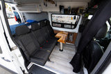 Inside a comfortable RV rental: custom van conversion with bench seats, dining table, bed, and beach view.