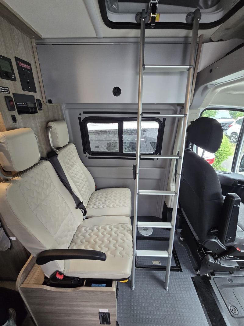 Inside an rv rental: cream passenger seats, essential control panels, and a sturdy ladder leading to an overhead sleeping area. — photo 8