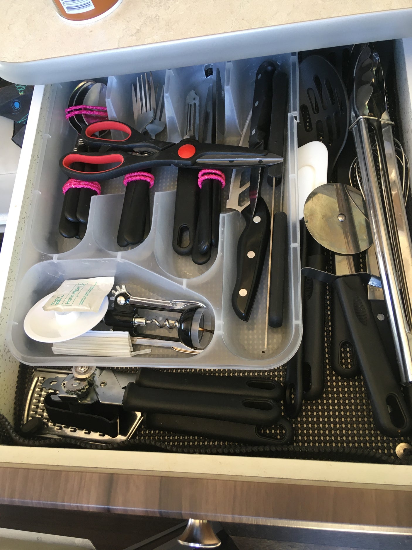 An RV rental kitchen drawer, neatly organized with a clear tray holding various cooking utensils, knives, and tools.