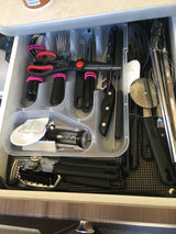 An RV rental kitchen drawer, neatly organized with a clear tray holding various cooking utensils, knives, and tools.